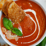 Bowl of tomato soup with bread, basil, and parmesan on top.
