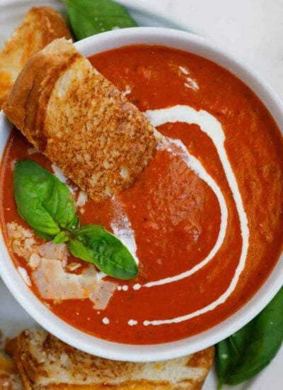 Bowl of tomato soup with bread, basil, and parmesan on top.