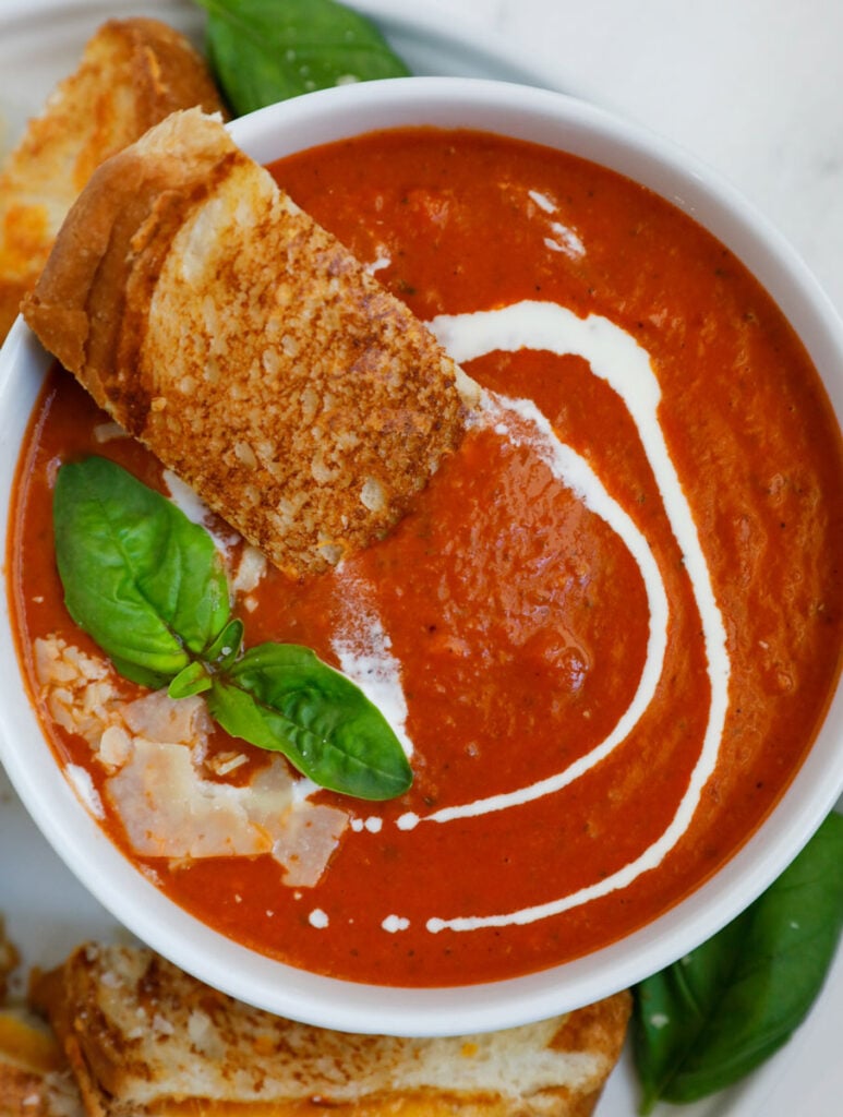 Bowl of tomato soup with bread, basil, and parmesan on top.