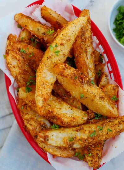 Top down view of crispy potato wedges in a red basket.