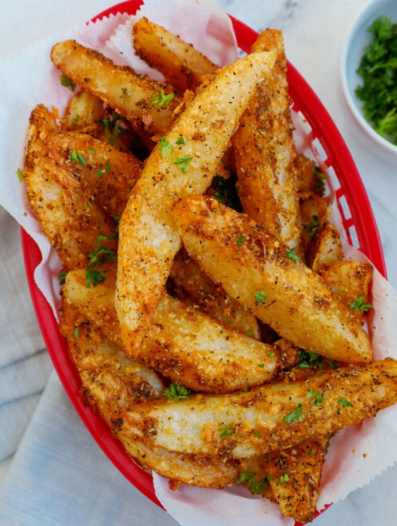 Top down view of crispy potato wedges in a red basket.