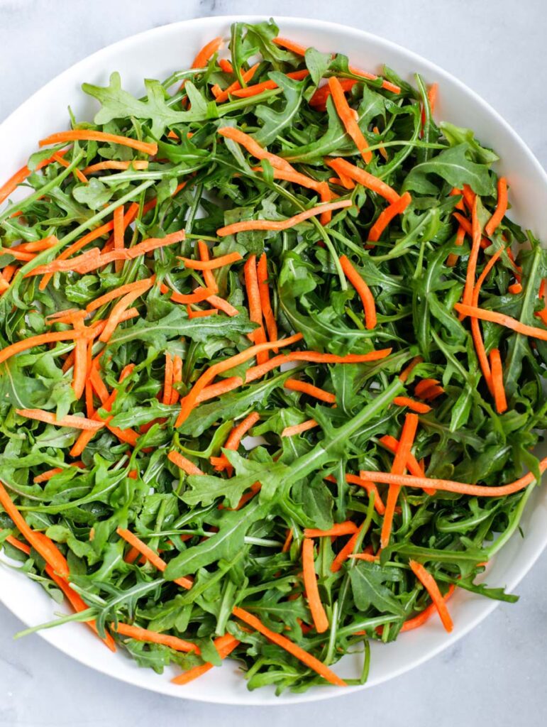 Arugula and shredded carrots in a bowl.