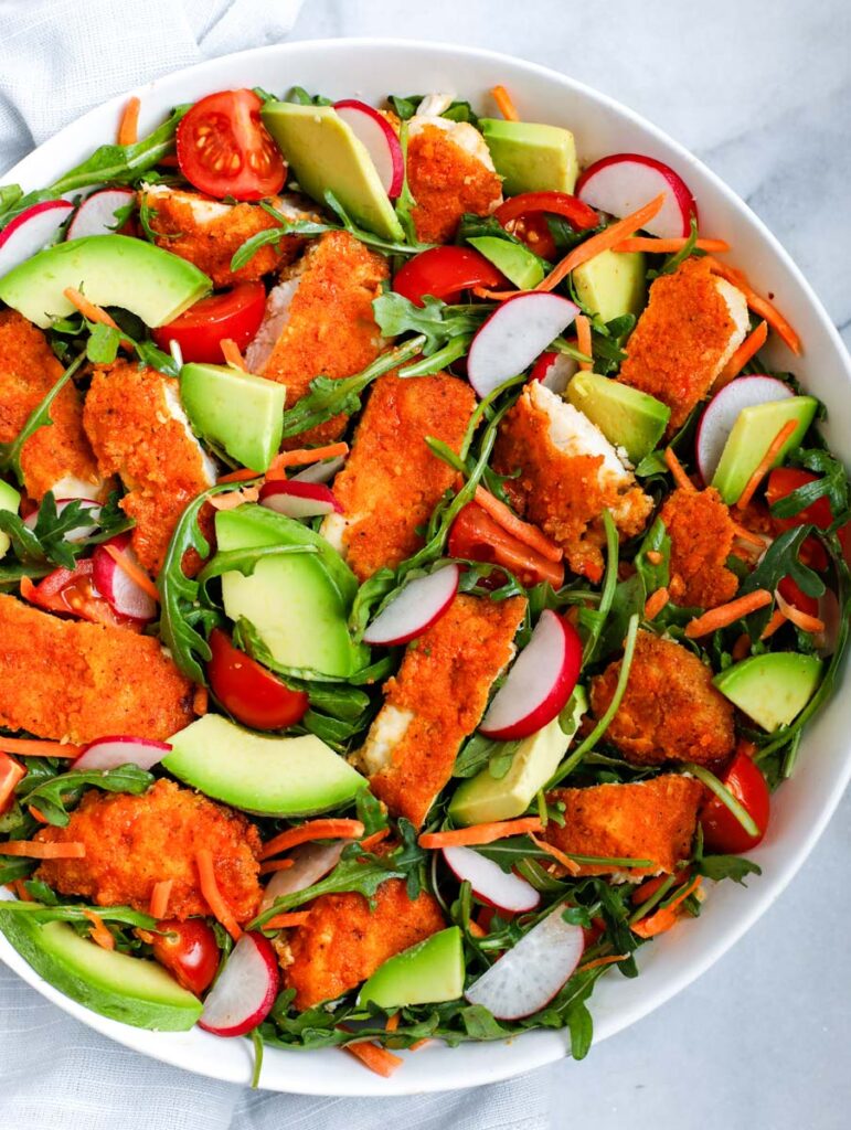 Arugula chicken and veggies in a white bowl.