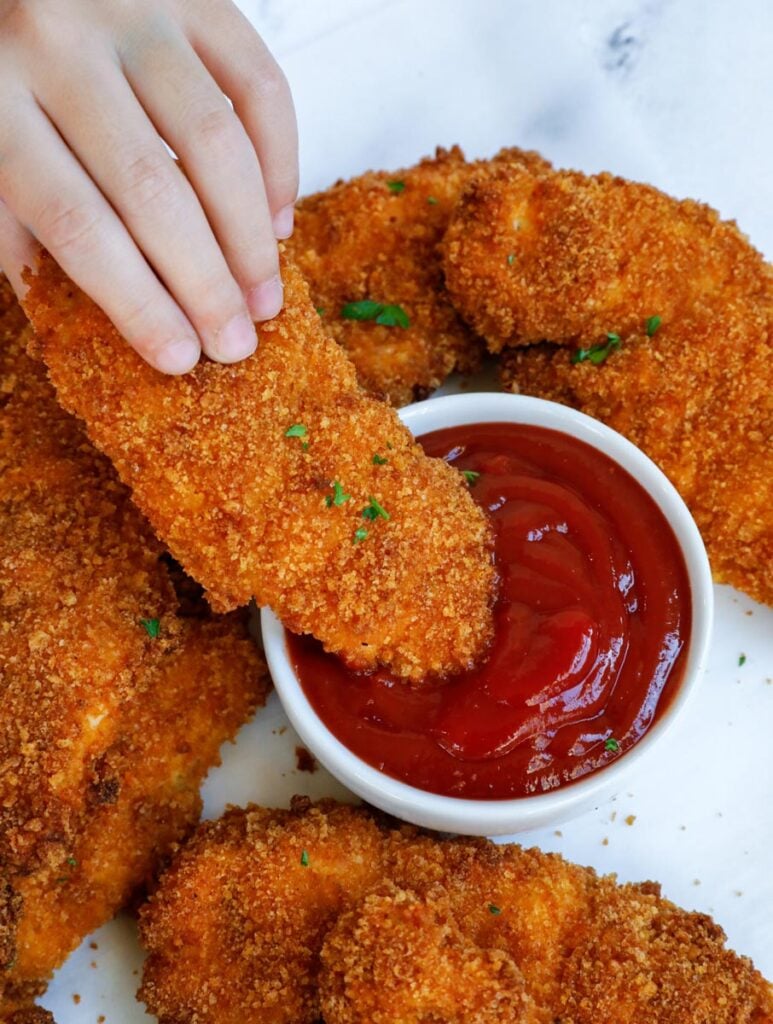 chicken tenders being dipped in ketchup