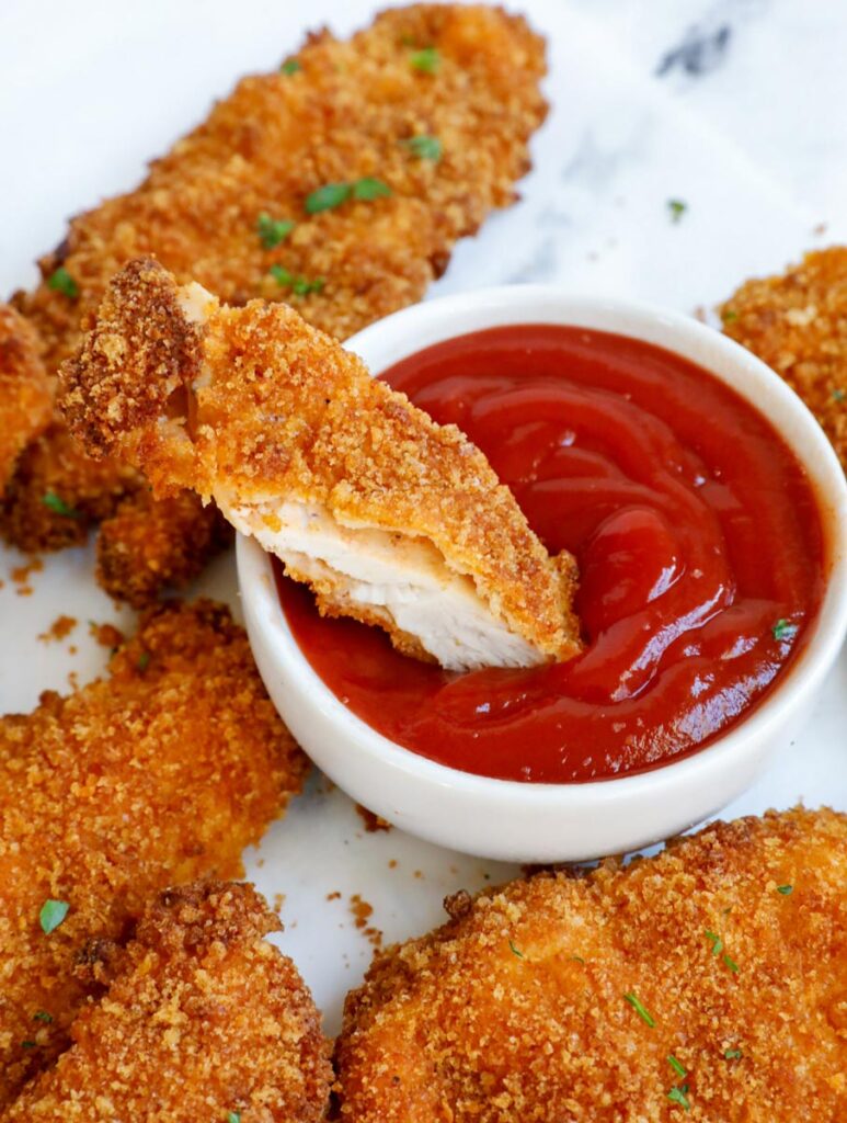 a piece of sliced chicken tenders being dipped into ketchup