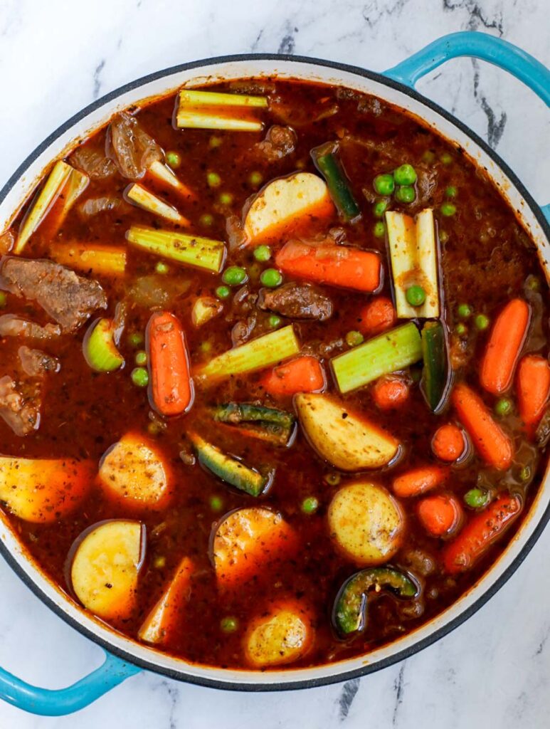 Top down view of beef and vegetables in a blue pot.