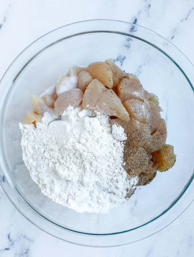 Chicken being added to a bowl with flour, salt, and pepper.