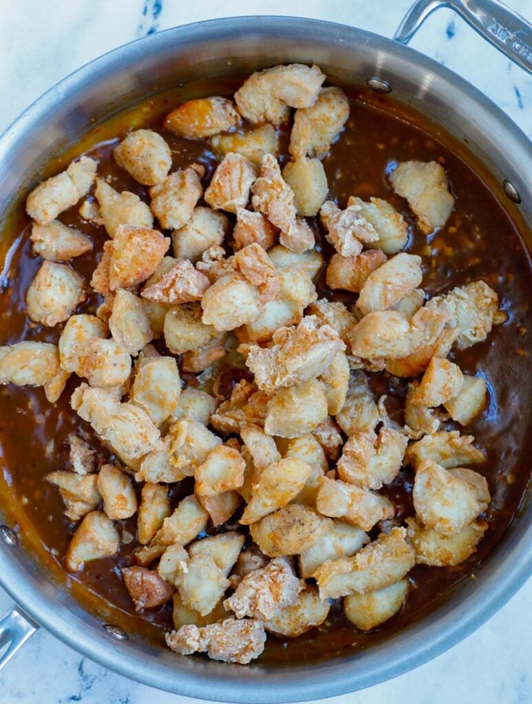 Chicken being added into sauce in a skillet.