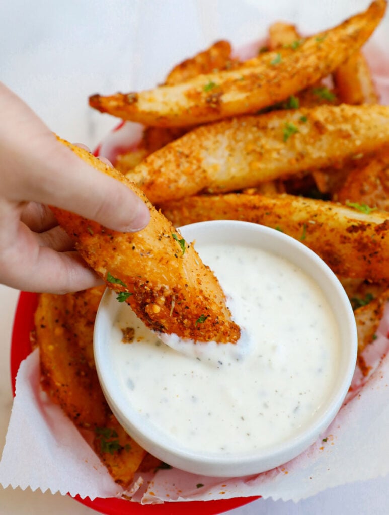 Hand dipping a potato wedge into some sauce. 