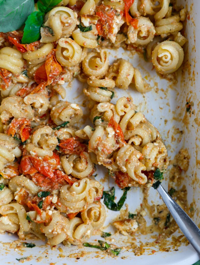 Feta pasta in a white casserole dish being spooned out.