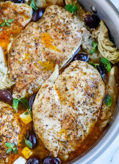 Overhead shot of greek chicken in a skillet with olives and artichokes.