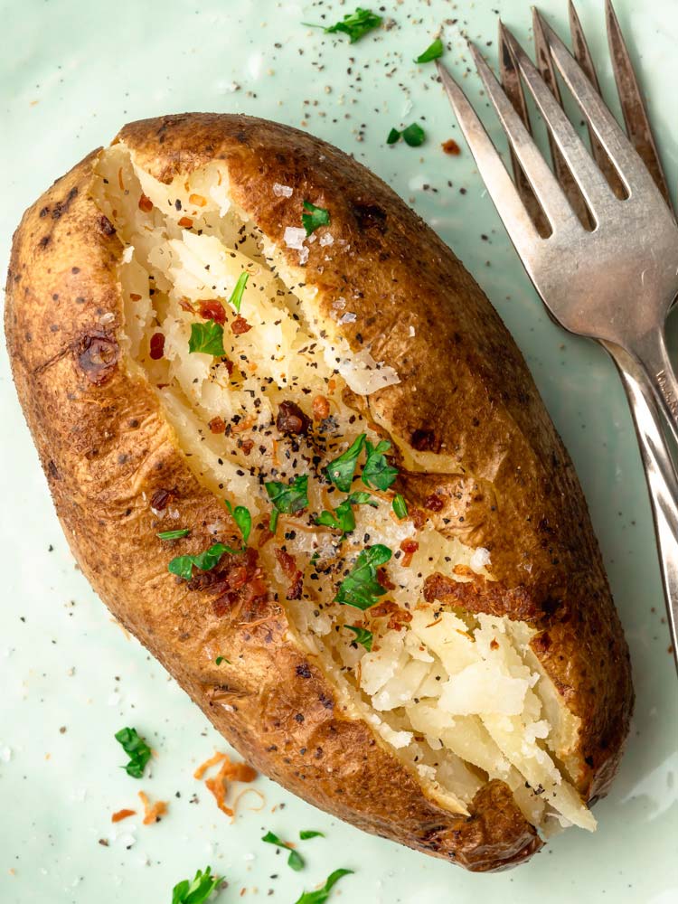 baked potato on a plate topped with bacon, parsley and black pepper