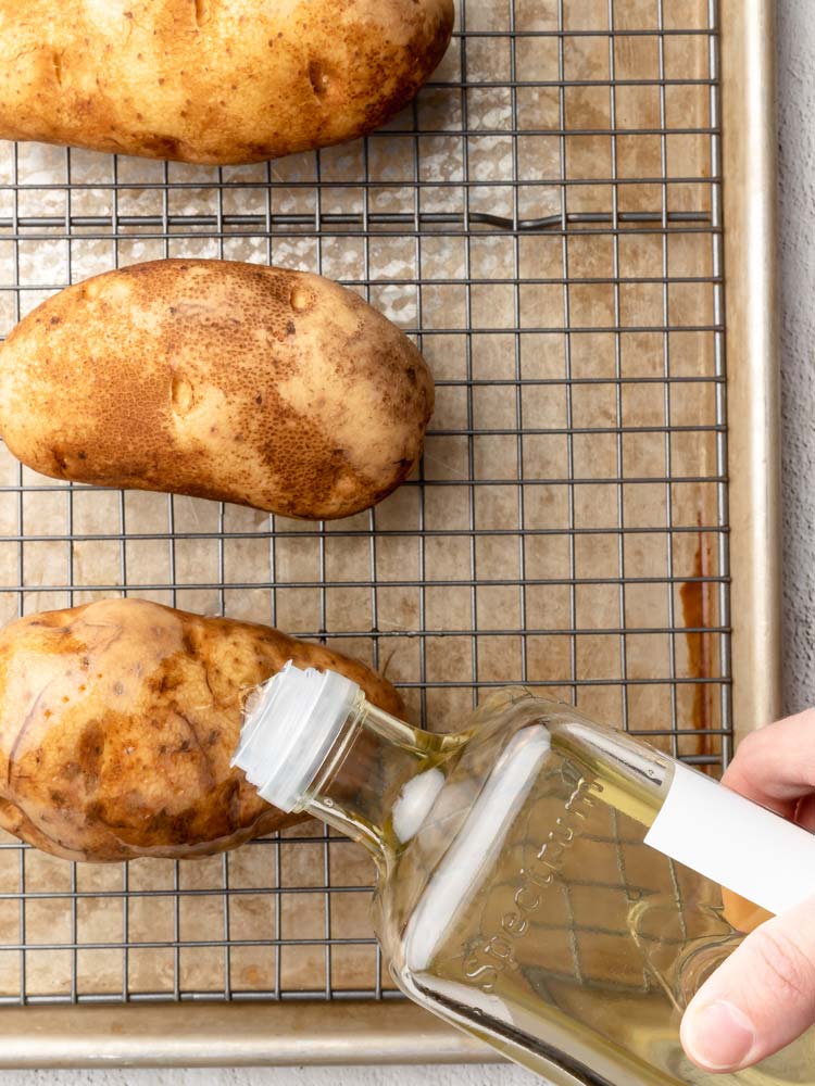 olive oil being drizzled on a potato before baking