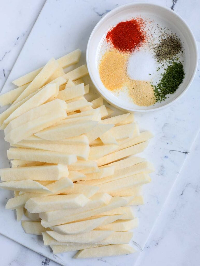 Sliced jicama on a marble countertop with a bowl of spices.