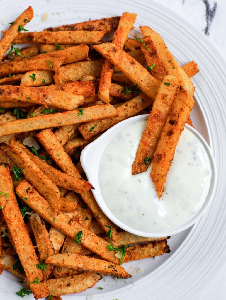 Overhead shot of jicama fries on a white plate with yogurt dip. 