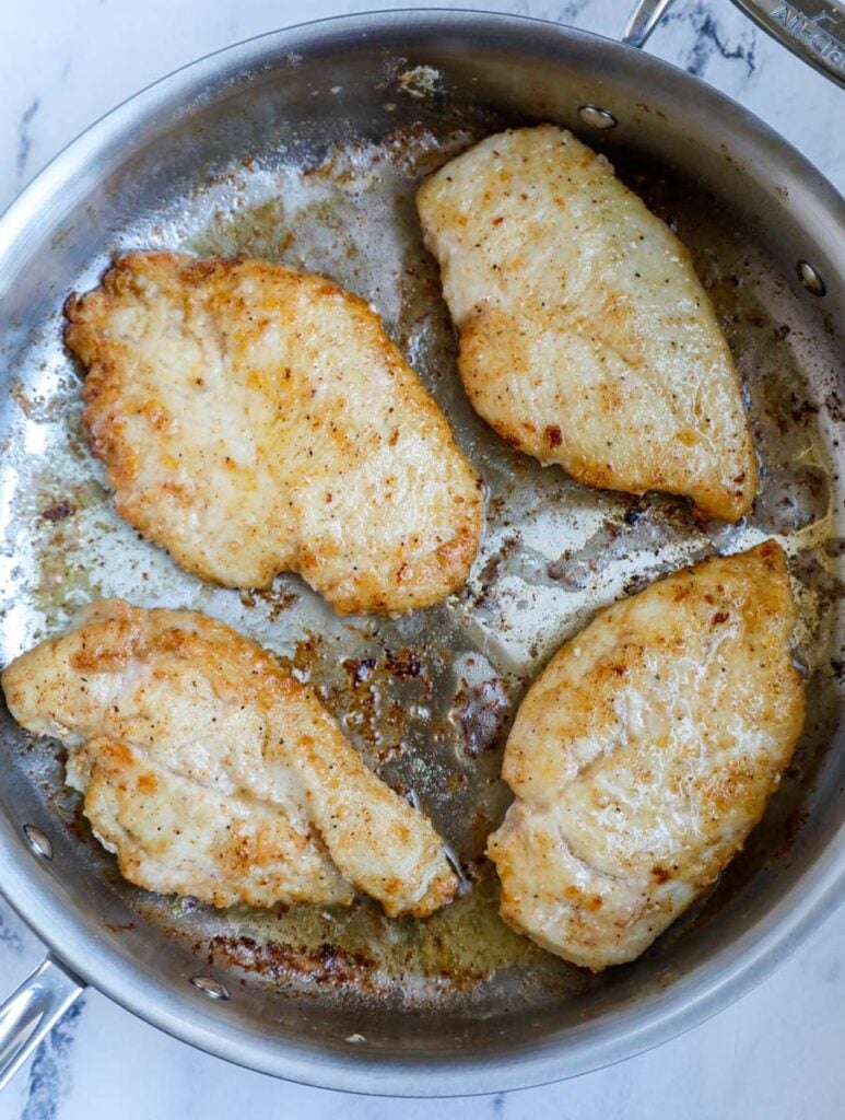 Top down view of chicken breasts in a skillet.