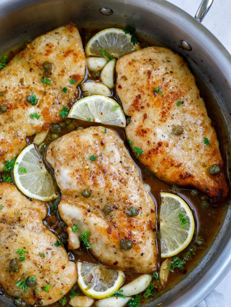 Overhead shot of lemon chicken piccata in a pot with lemon wedges.