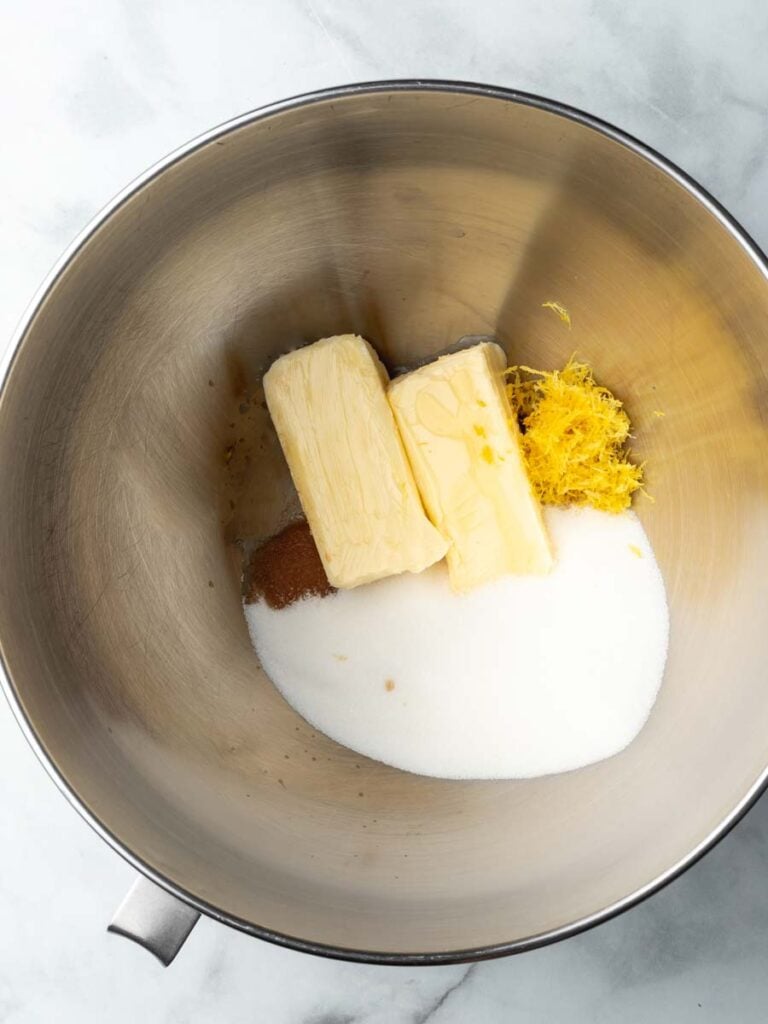 A mixing bowl with sugar, butter, lemon zest, and vanilla extract.