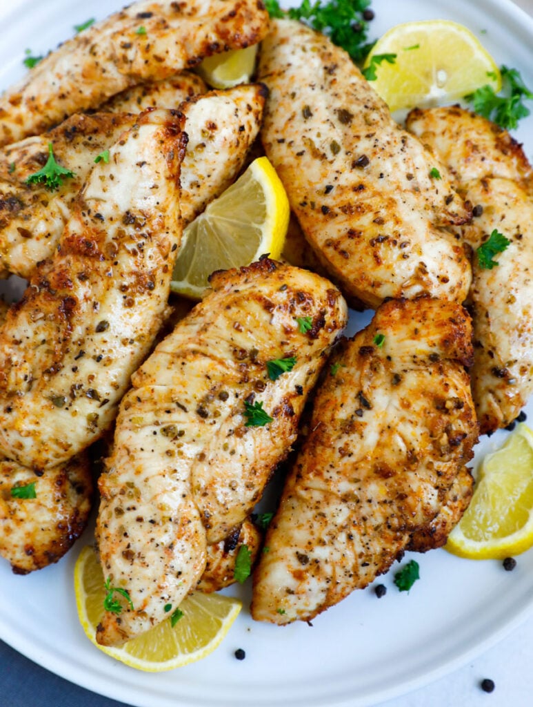 Top down shot of lemon pepper chicken on a plate with lemon wedges.