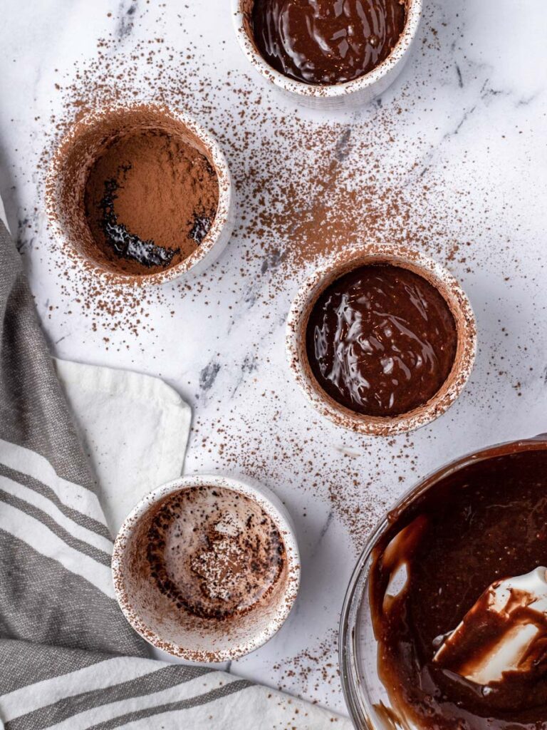 Multiple ramekins dusted with powder and 2 filled with batter.