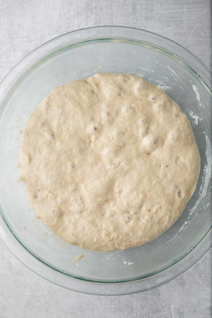 Dough rising with bubbles in it in a glass bowl.