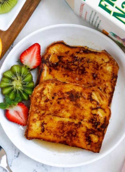 Orange french toast on a plate served with a kiwi and sliced strawberry.