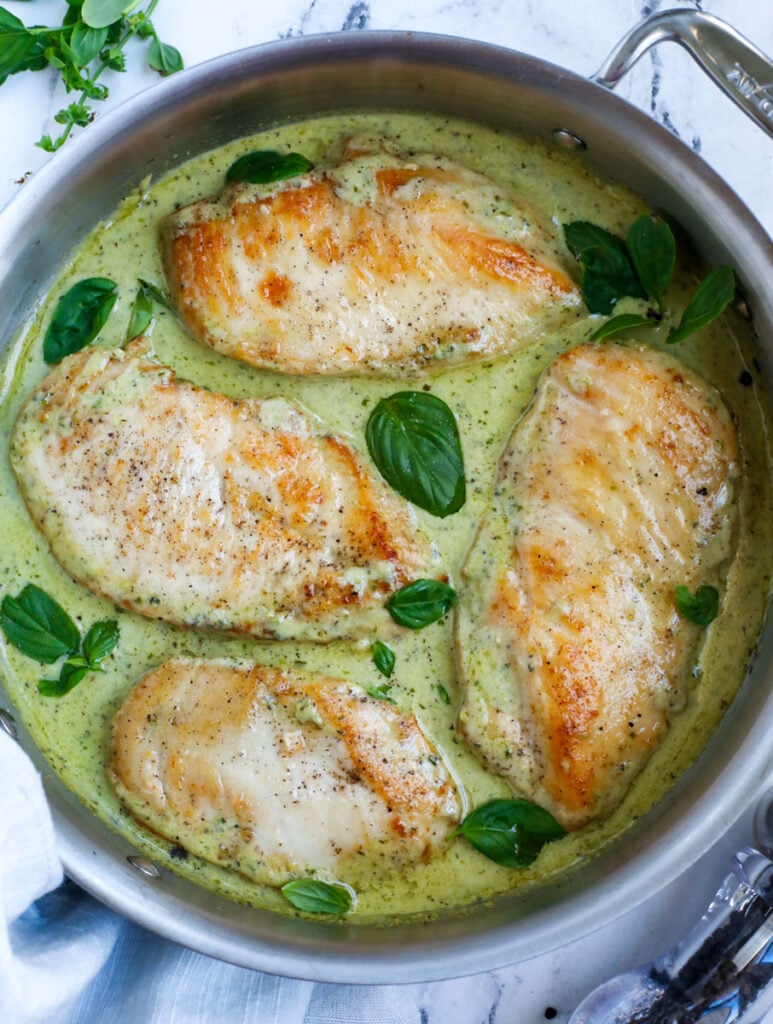 Top down view of creamy pesto chicken in a pan.