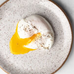 poached egg on a plate, yolk cut through and seasoned with black pepper