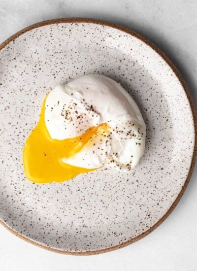 poached egg on a plate, yolk cut through and seasoned with black pepper