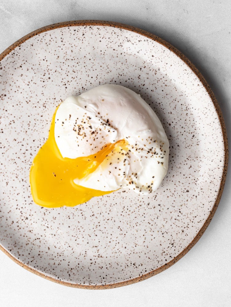 poached egg on a plate, yolk cut through and seasoned with black pepper