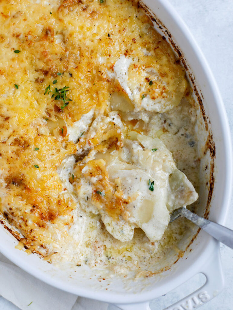 Top down shot of potatoes gratin with spoon in a white baking dish.