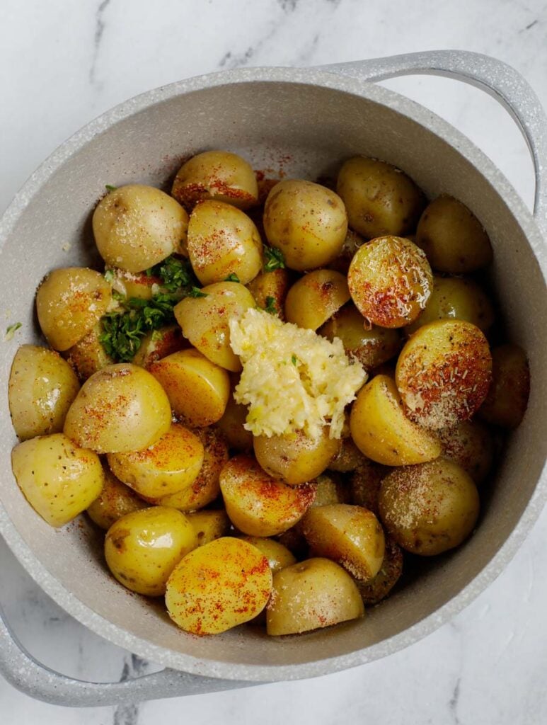 Top down shot of potatos being mixed with herbs garlic and olive oil.