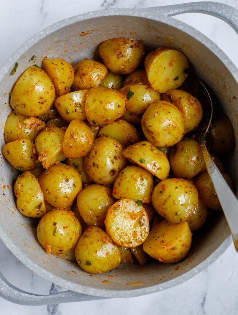 Potatoes covered in olive oil being mixed with a spoon in a white bowl. 
