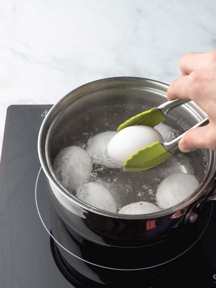 an egg being removed from the pot with a tong