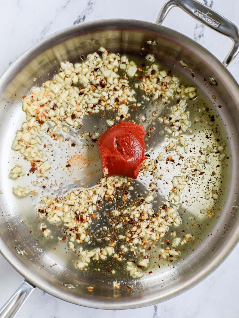Top down shot of tomato paste in pot with aromatics.
