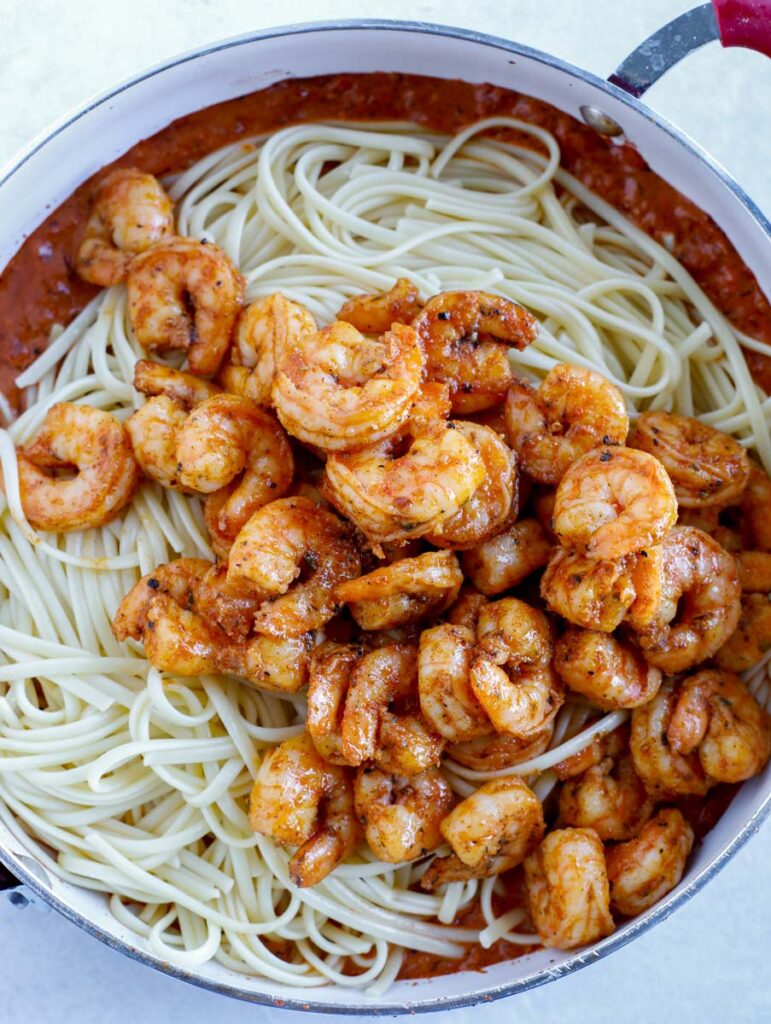 Shrimp on top of noodles in a skillet.