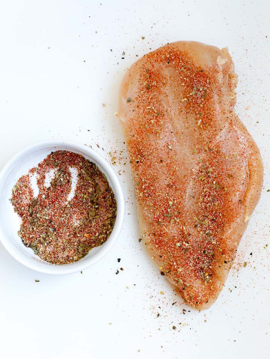 Top down shot of raw chicken breast with seasoning on it. 