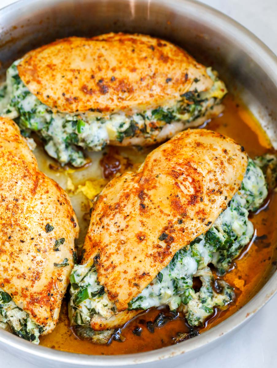 Side shot of three spinach stuffed chicken breasts in a pan.