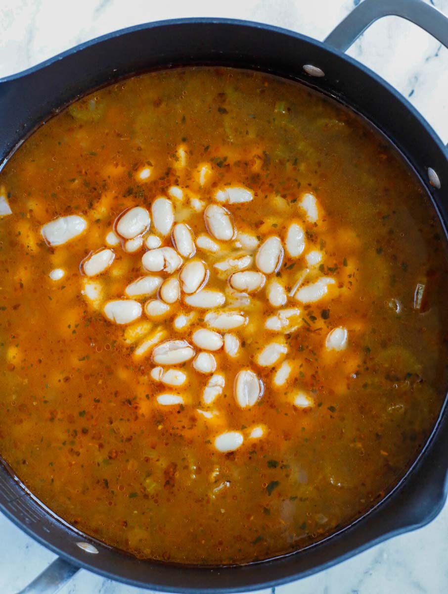 White beans being added to a pot of soup.