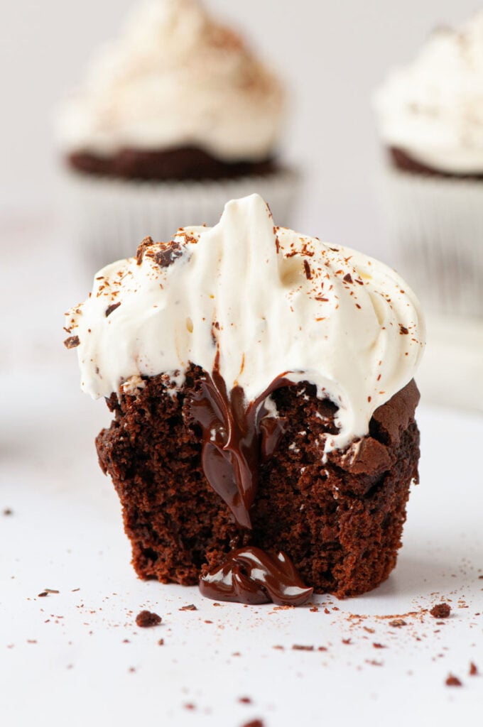 chocolate cupcake with whip cream on top and chocolate in the middle and a bite taken out of it