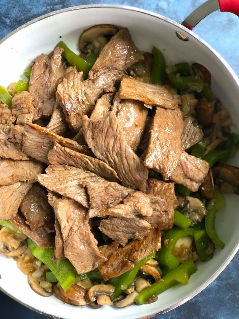 Steak, peppers, mushrooms and onions in a white skillet