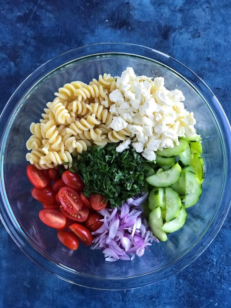 Greek Pasta Salad ingredients - feta cheese, pasta, cucumbers, tomatoes, onion, and fresh parsley 