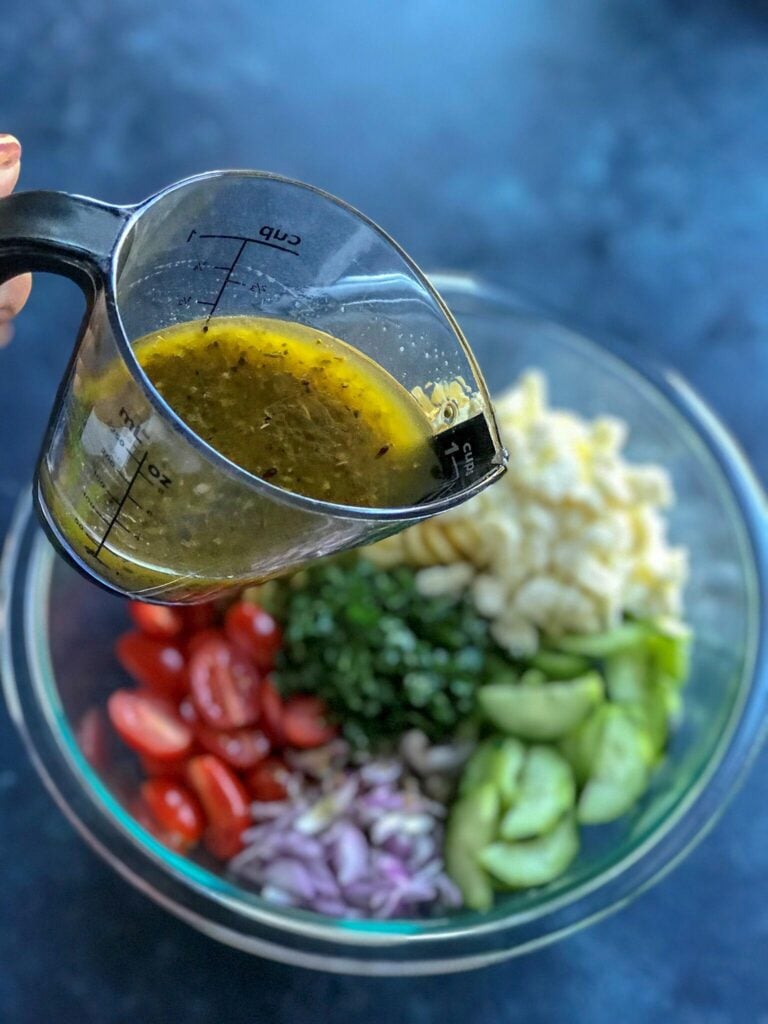 Pouring lemon vinaigrette on the pasta salad ingredients 