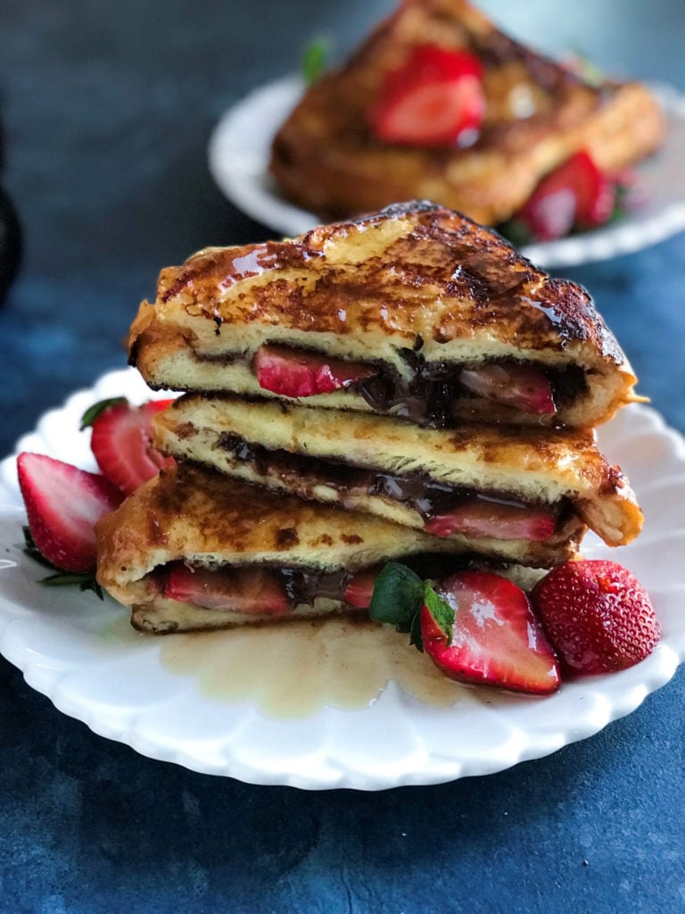 Side shot of strawberry nutella french toast on a plate with strawberries on the side. 