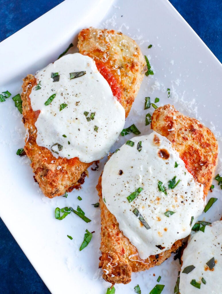 Overhead shot of Baked chicken parm with cheese and basil topping