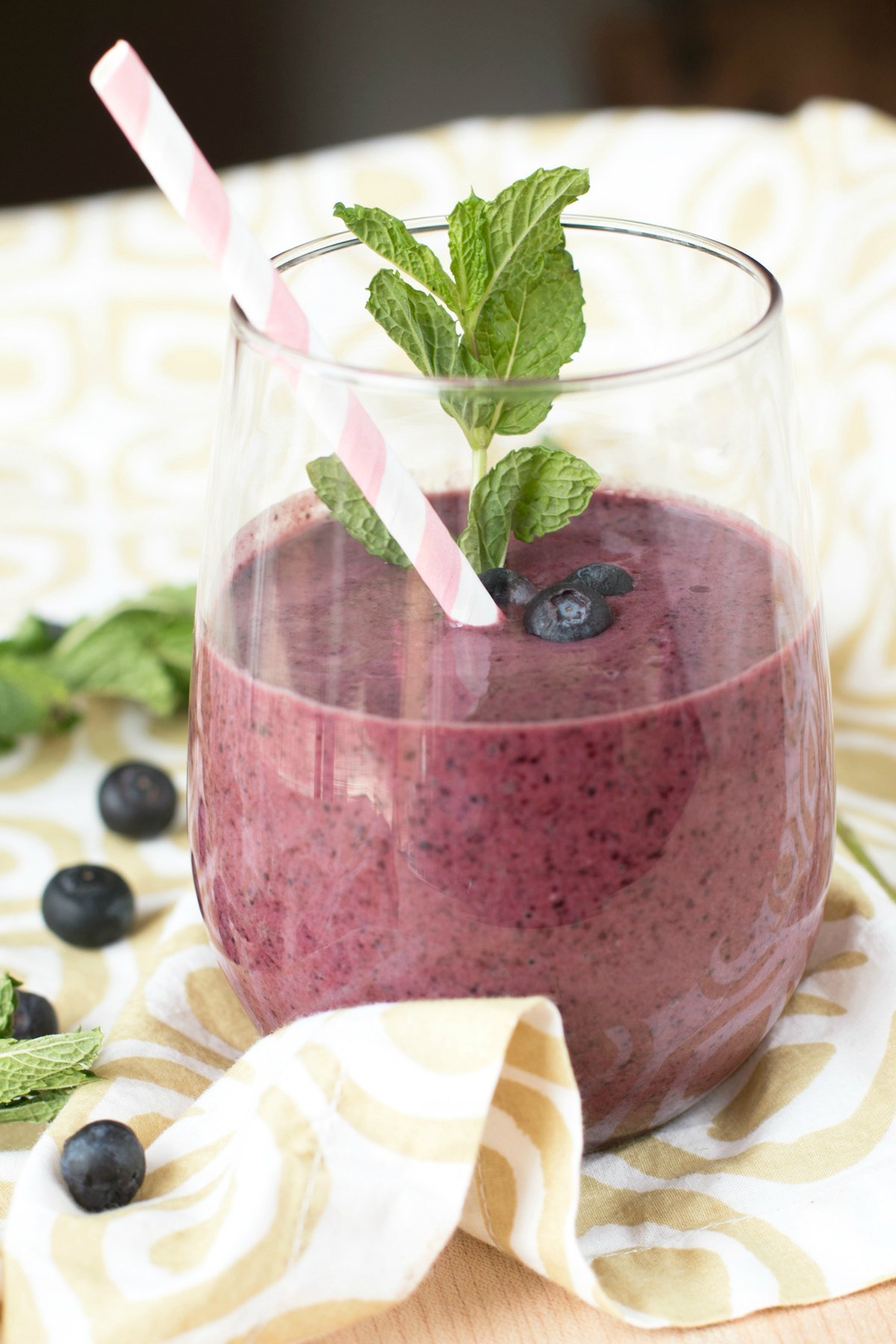 A small glass filled with a blueberry smoothie with mint and sitting on a tan floral cloth napkin