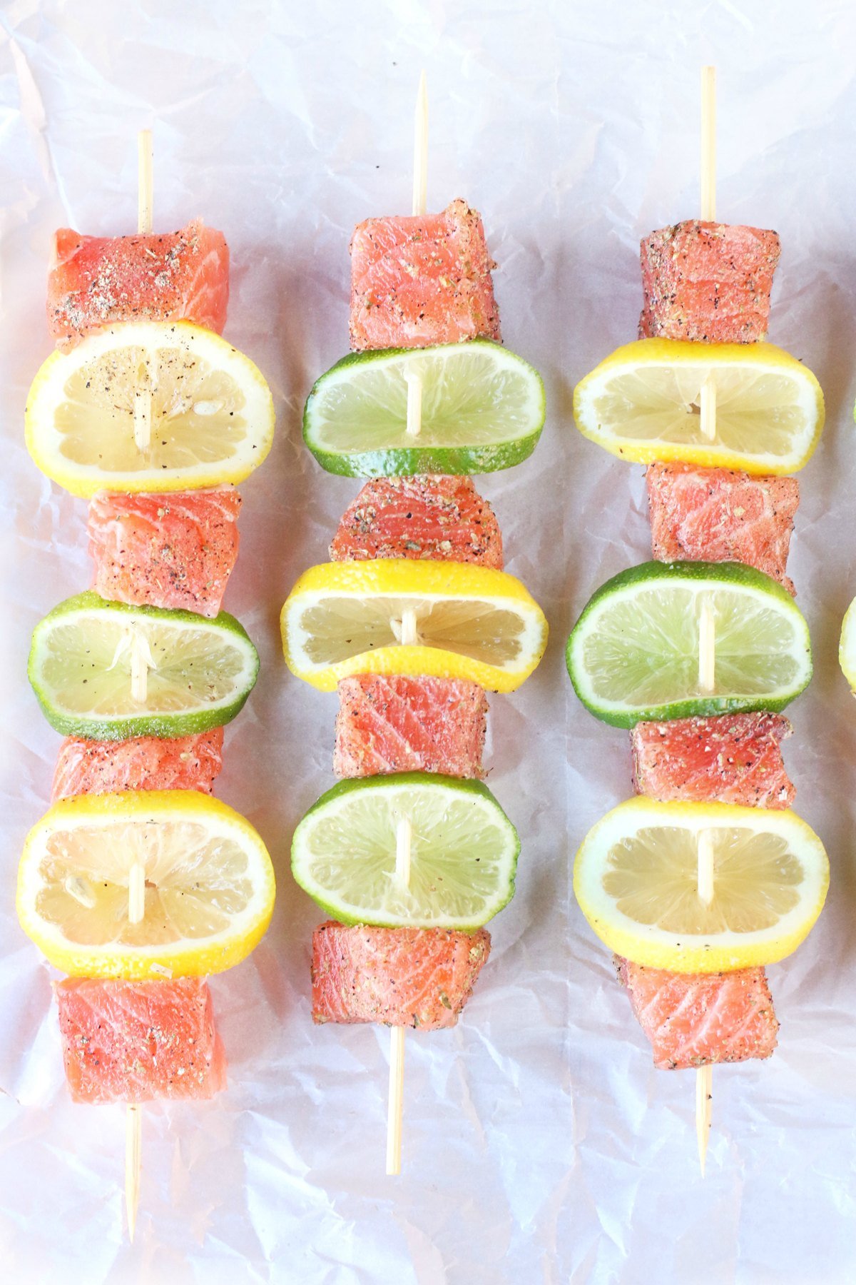 Fresh salmon skewers with lemon and lime laying on a lined pan ready to grill