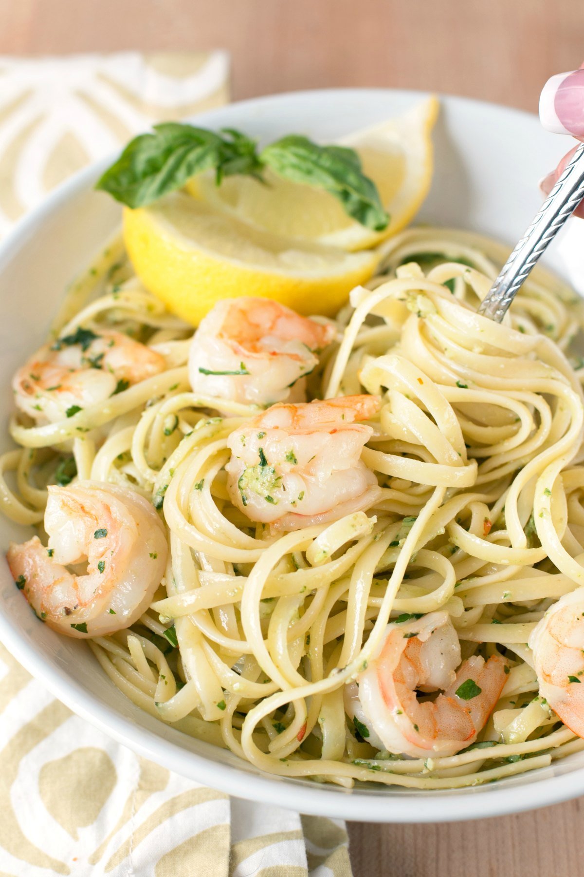 Overhead picture of a large white bowl of pasta with pesto shrimp scampi and lemon slices