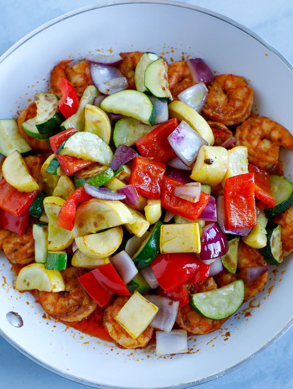 sautéed veggies over cooked shrimp in a white skillet.