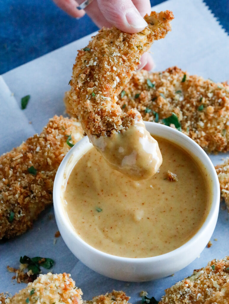 Baked Parmesan Chicken Tenders hand holding Baked Parmesan Crusted Chicken